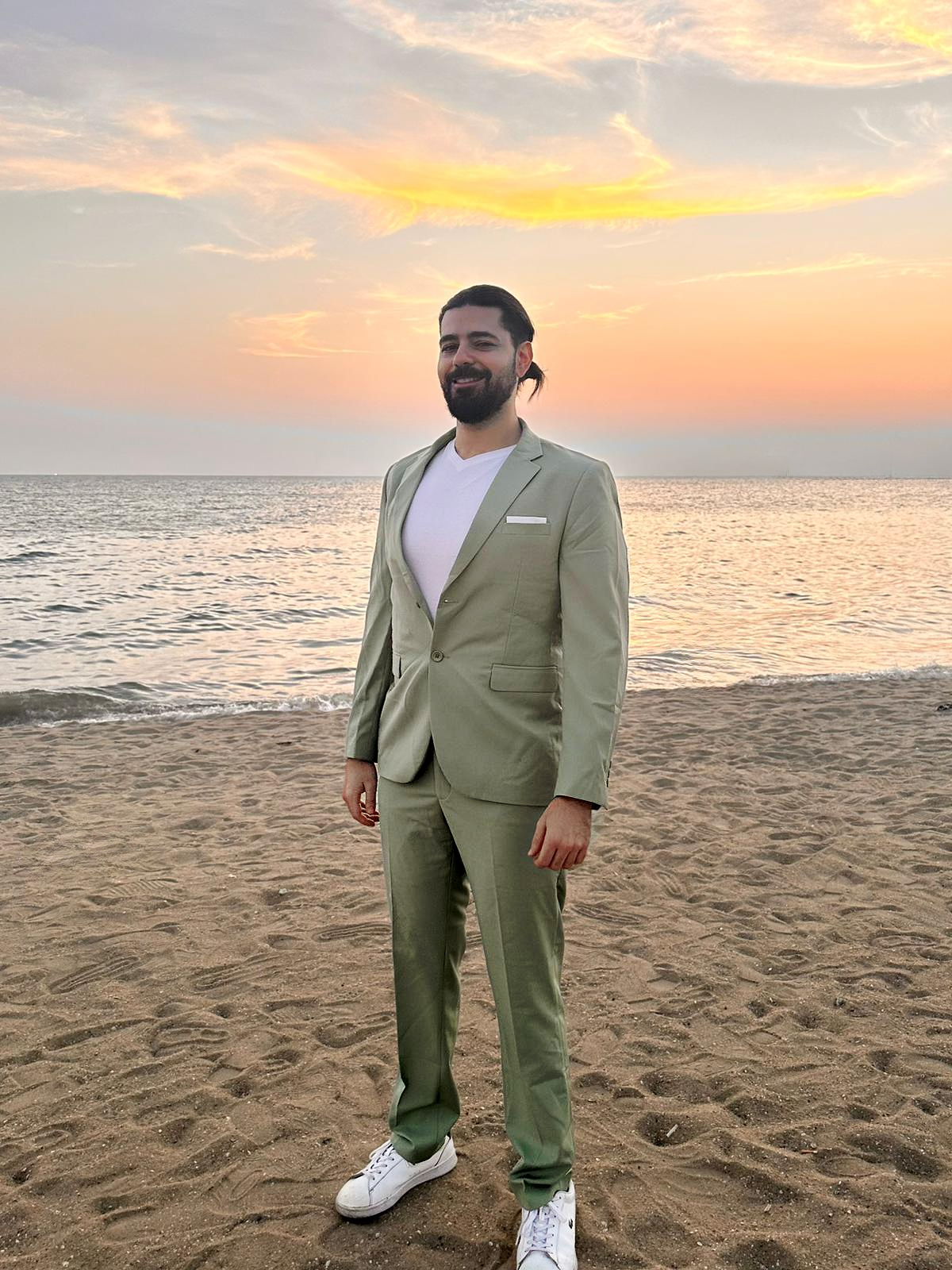 Yan London in an olive suit on a beach at sunset